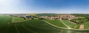 Panoramaluftbild von Isserstedt: im Vordergrund sieht man grüne Ackerflächen gefolgt von der Siedlung mit Häusern auf der rechten Seite und auf der linken Seite sieht man das Gewerbegebiet, gefolgt von grünen Ackerflächen