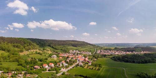 Panoramaluftbildaufnahme von Ilmnitz: Im Vordergrund ist die Siedlung mit Häusern umgeben von grünen Ackerflächen, Waldflächen und Bergen