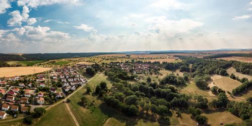 Luftbildaufnahme von Münchenroda: im Vordergrund sind grüne Ackerflächen sowie kleine Waldstücke, gefolgt von der Siedlung mit Häusern, dann folgen Ackerflächen sowie Waldlandschaften