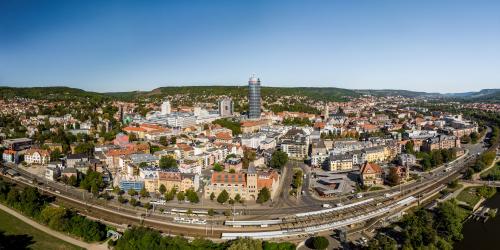 Luftbildaufnahme von Jena-Zentrum aus Südrichtung: Im Vordergrund ist der Stadtpark Paradies gefolgt vom Paradies-Bahnhof, dann folgt die Innenstadt mit vielen Häusern, der Jentower und anschließend der Landgraf