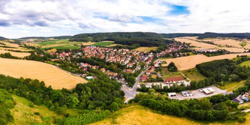 Luftbildaufnahme von Jenaprießnitz/Wogau: Im Vordergrund sind grüne Ackerflächen sowie landwirtschaftliche Nutzflächen gefolgt von der Siedlung mit Häusern, dann folgen grüne Ackerflachen, landwirtschaftliche Nutzflächen und Waldflächen
