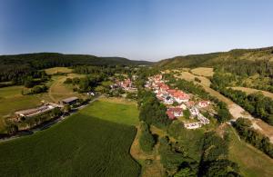 Luftbildaufnahme von Leutra aus Richtung Nord-Ost: Im Vordergrund sind grüne Ackerflächen, gefolgt von der Siedlung mit Häusern, welche von grünen Wald- und Ackerflächen umgeben ist, gefolgt von bergiger Landschaft