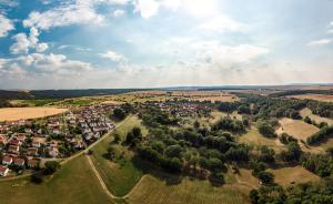 Luftbildaufnahme von Münchenroda: im Vordergrund sind grüne Ackerflächen sowie kleine Waldstücke, gefolgt von der Siedlung mit Häusern, dann folgen Ackerflächen sowie Waldlandschaften