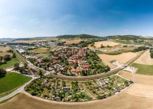 Luftbildaufnahme Maua: Im Vordergrund sind landwirtschaftliche Nutzflächen, gefolgt von einer Kleingartenanlage, dahinter Bahngleisen, gefolgt von der Siedlung mit Häusern, auf der linken Seite ist das Gewerbegebiet und auf der rechten Seite sind landwirtschaftliche Nutzflächen sowie die Autobahnauffahrt A4 Richtung Dresden oder Frankfurt/Main, im Hintergrund ist der Ortsteil Leutra sowie eine bergige Landschaft