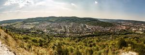 Blick vom Jenzig auf Wenigenjena: im Vordergrund ist das Gebirge mit Büschen und Bäumen, gefolgt von der großen Siedlung mit Häusern, gefolgt vom Hausberg mit Fuchsturm; auf der rechten Seite mittig vom Bild liegt das Zentrum Jenas und auf der linken Seite am Ende der Siedlung sind landwirtschaftliche Nutzflächen