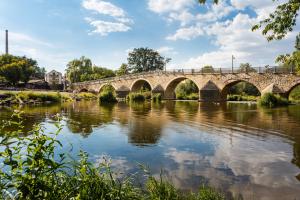 Aufnahme von der Burgauer Brücke am Wehr: Im Vordergrund ist der Fluss die Saale, gefolgt von der historischen Natursteinbrücke mit Gewölbe