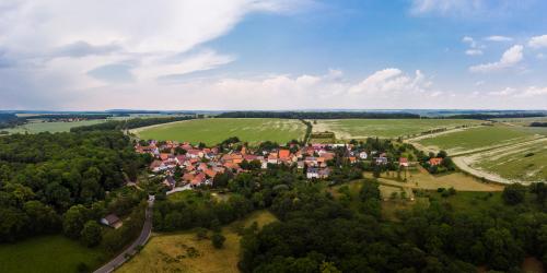 Luftbildaufnahme von Closewitz Richtung Weimar: im Vordergrund grüne Ackerflächen und kleine Waldlandschaften, gefolgt von der Siedlung mit Häusern, dann folgen grüne Ackerflächen und ein blauer Himmel mit Schleierwolken