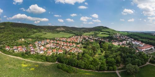 Luftbildaufnahme von Drackendorf: im Vordergrund sind grüne Wiesen und der Park von Drackendorf, gefolgt von der Siedlung mit Häusern und den Kernbergen im Hintergrund