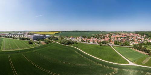 Panoramaluftbild von Isserstedt: im Vordergrund sieht man grüne Ackerflächen gefolgt von der Siedlung mit Häusern auf der rechten Seite und auf der linken Seite sieht man das Gewerbegebiet, gefolgt von grünen Ackerflächen