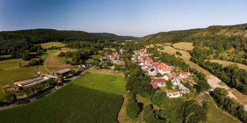 Luftbildaufnahme von Leutra aus Richtung Nord-Ost: Im Vordergrund sind grüne Ackerflächen, gefolgt von der Siedlung mit Häusern, welche von grünen Wald- und Ackerflächen umgeben ist, gefolgt von bergiger Landschaft